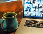 Photographie d??un ordinateur présentant un écran de visioconférence. Une tasse verte posée sur une table en bois.